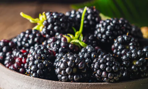 Brombeeren in einer Schale neben einem Glas Fruchtaufstrich